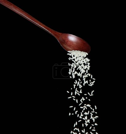 Téléchargez les photos : Japanese Rice fall, white grain rices versing down abstract cloud fly from spoon. Belle graine complète de riz dans l'air, design objet alimentaire. Mise au point sélective prise de vue au gel Fond noir isolé - en image libre de droit