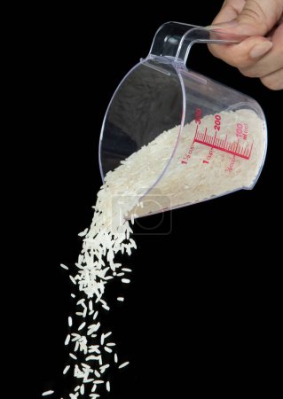 Foto de Otoño de arroz japonés, arroz de grano blanco vertiendo una nube abstracta que vuela de la taza de medición. Hermoso arroz de semilla completa en el aire, diseño de objetos alimenticios. Congelación de enfoque selectivo tiro Fondo negro aislado - Imagen libre de derechos