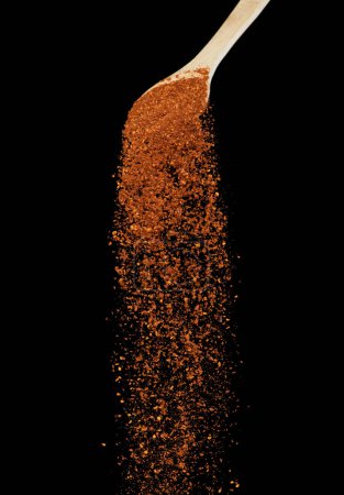 Foto de Red Hot Chilli caída, rojo grano chile explotar nube abstracta volar de cuchara de madera. Hermosa semilla completa fría, diseño de objetos alimenticios. Congelación de enfoque selectivo tiro fondo negro aislado - Imagen libre de derechos