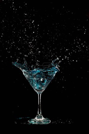 Téléchargez les photos : Verre à cocktail bleu avec éclaboussures d'alcool d'eau, éclaboussures de boisson Crystal Cocktail dans l'air et bulle de verre. Liquor Part gel tourné à grande vitesse sur fond noir isolé - en image libre de droit