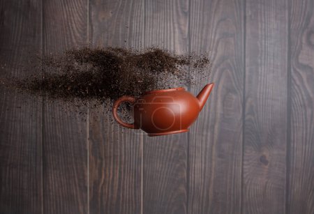 Photo for Black dried leave Tea fly in Pot. Small Fine size tea leaf flying explosion, Abstract cloud fly. Brown colored Teas pot splash throwing in Air. Wooden background Isolated high speed freeze - Royalty Free Image