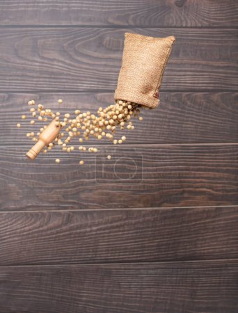 Foto de Soy Bean flying explosion in sack bag, yellow grain beans explode abstract cloud fly. Beautiful complete seed pea soy bean sack bag splash in air, food object design. Wooden background isolated freeze - Imagen libre de derechos