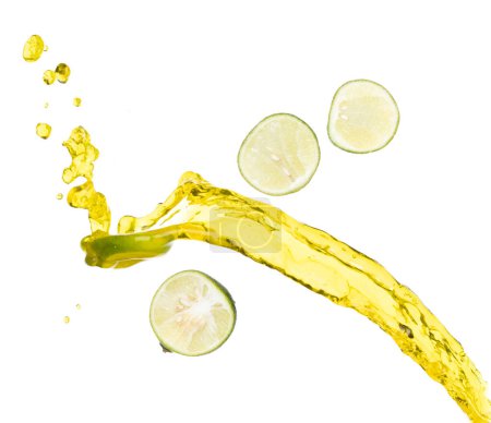 Téléchargez les photos : Verser le jus de citron vert dans le verre, le jus de citron vert tombe dans l'eau liquide jaune. Trancher le citron vert dans le jus jeter éclaboussure dans l'air. Fond blanc Obturateur haute vitesse isolé, action de gel - en image libre de droit