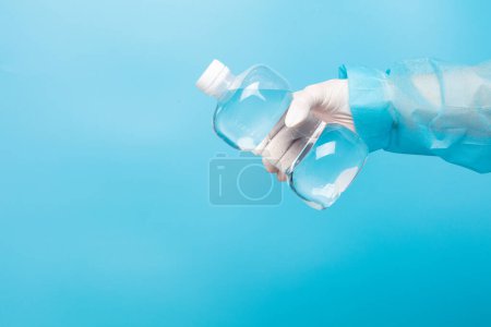 Photo for Saline medical cleaning normal solution plastic bottle in hand of nurse with glove, clear of normal saline in plastic bottle to clean nose sterile medical equipment over blue background isolated - Royalty Free Image