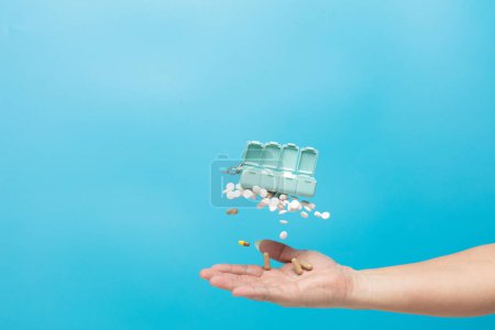 Photo for Daily pill drug medicine box container falling down to patient hand. Many kind of drugs pills medicines to help patient fly to senior hand. Drug pill Medical over blue background isolated - Royalty Free Image