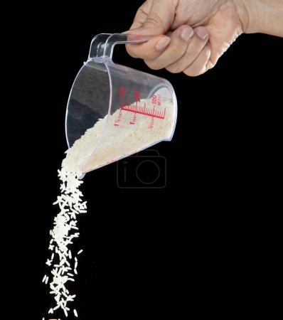 Foto de Otoño de arroz japonés, arroz de grano blanco vertiendo una nube abstracta que vuela de la taza de medición. Hermoso arroz de semilla completa en el aire, diseño de objetos alimenticios. Congelación de enfoque selectivo tiro Fondo negro aislado - Imagen libre de derechos