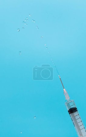 Photo for Syringe inject serum cure drug from needle tube and fly in air. Syringe push up testing and get rid of oxygen air in tube out. Syringe with sharp needle in hand. Medical over blue background isolated - Royalty Free Image