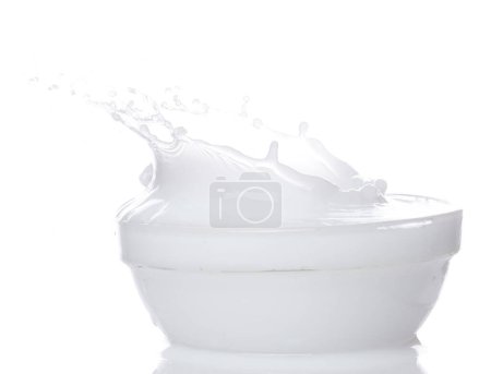 Téléchargez les photos : Le yaourt au lait déverse de l'eau blanche dans le bol. Lait lotion verser flotter dans l'air milieu. Lait hydratant explosion jeter flottement. fond blanc isolé haute vitesse obturateur gel mouvement - en image libre de droit