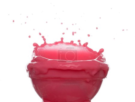 Foto de El jugo de fresa de tomate rojo se derrama en un recipiente de vidrio, la ola de sangre roja cae en el aire. Una explosión de color vino tinto se derrama. Fondo blanco Obturador de alta velocidad aislado, movimiento de congelación - Imagen libre de derechos