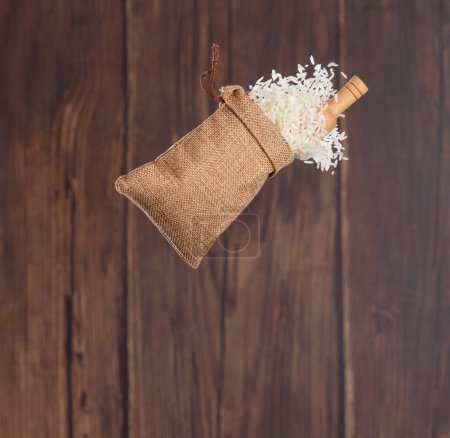 Foto de Japanese Rice in sack bag flying explosion, white grain rices fall abstract fly. Beautiful complete seed rice bag splash in air, food object design. Wood kitchen background, high speed freeze motion - Imagen libre de derechos