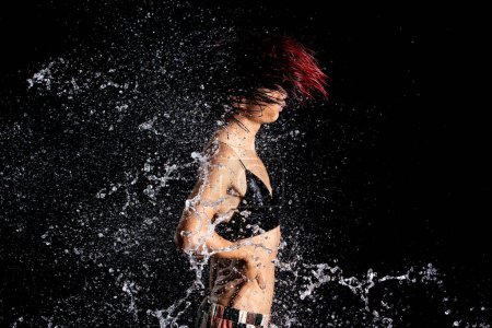 Foto de Piel bronceada Mujer asiática en bikini posa en aqua studio. Salpicaduras Las gotas de agua se esparcen al cuerpo. Emoción divertida chica femenina en el ataque de agua revoloteando y detener el movimiento de congelación disparo, fondo negro aislado - Imagen libre de derechos