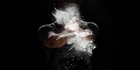 Photo for Chef prepare white flour dust for cooking bakery food. Elderly man Chef clap hand, white flour dust explode fly in air. Flour stop motion in air with freeze high speed shutter, black background - Royalty Free Image