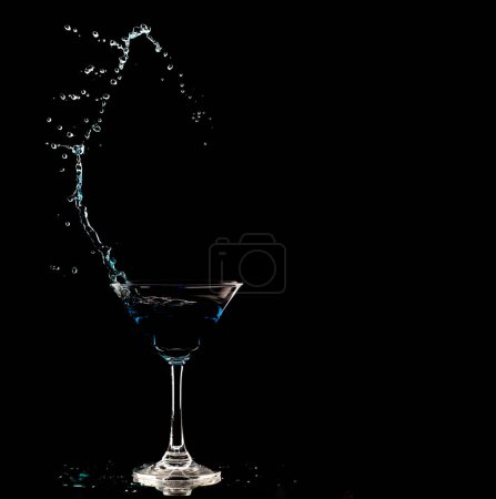 Photo for Blue Cocktail Glass with splashing water alcohol, Crystal Cocktail drink splatter splash in air and bubble from glass. Liquor Part freeze shot high speed over black background isolated - Royalty Free Image