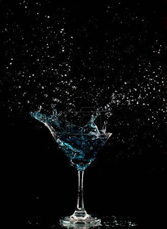 Foto de Azul vaso de cóctel con salpicaduras de alcohol de agua, cristal cóctel bebida salpicadura salpicadura en el aire y burbuja de vidrio. Licor Parte congelación disparo de alta velocidad sobre fondo negro aislado - Imagen libre de derechos