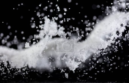Téléchargez les photos : Poudre de sel verser tomber dans un bol, blanc Cristal de sel cuire mouche nuage abstraite. Éclaboussure de sel moulu dans l'air, conception d'éléments alimentaires. Fond noir isolé foyer sélectif flou - en image libre de droit