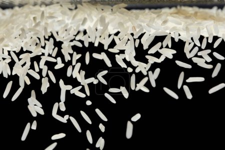 Foto de Explosión voladora de arroz japonés, los arroces de grano blanco caen mosca abstracta. Hermosa semilla completa de arroz de jazmín salpicadura en el aire, diseño de objetos alimenticios. Fondo negro aislado enfoque selectivo borroso - Imagen libre de derechos
