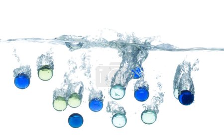 Téléchargez les photos : Boule de verre coloré tombe dans l'eau et crée des bulles d'air sur la surface. Goutte de boule de verre coloré frappé smash pour nettoyer l'eau et profonde à bulle. fond blanc isolé mouvement de gel - en image libre de droit