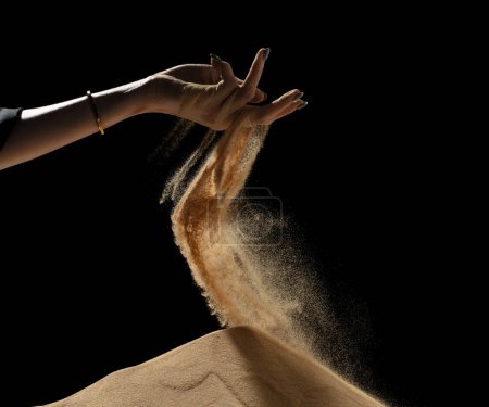 Photo for Hand releasing dropping sand on hill. Fine Sand flowing pouring through fingers hand against black background. Summer sand hill beach holiday vacation and time passing concept. Isolated freeze shot - Royalty Free Image