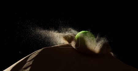 Photo for Tennis ball throw hit sand soil and Deep impact on sand hill and splash all over area. Tennis ball hit Sand dune hill over wind storm and blast dust splash over mountain. Black background isolated - Royalty Free Image