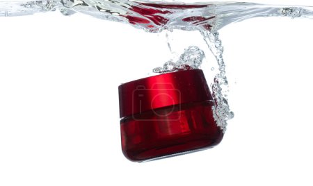 Téléchargez les photos : Récipient cosmétique rouge tomber dans l'eau claire avec bulle d'air. Conteneur de traitement cosmétique goutte à goutte à l'eau claire de fraîcheur. Blanc fond isolé élément de congélation - en image libre de droit