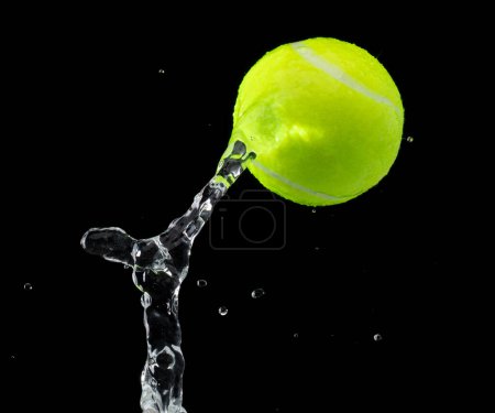 Foto de La pelota de tenis golpeó el agua y salpicó en el aire. La pelota de tenis verde vuela bajo la lluvia y salpica salpicaduras en el agua de gotas. Fondo negro acción de congelación aislada - Imagen libre de derechos