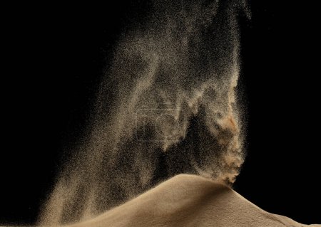 Téléchargez les photos : Le vent souffle sur la colline de sable et éclaboussure voler dans l'air. Colline de dunes de sable sur tempête de vent et éclaboussure de poussière de souffle sur la montagne. Après-midi ensoleillé sur sable vent de colline souffler. Fond noir isolé - en image libre de droit