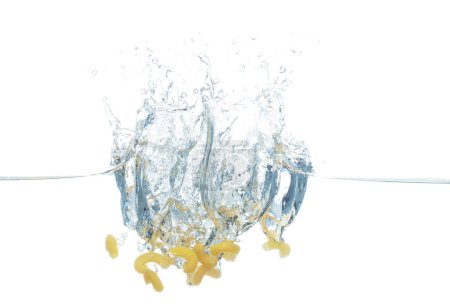 Photo for Raw pasta macaroni falls into water and creates air bubbles on surface. Yellow pasta macaroni drop hit smash to boil water and deep to bubble. White background isolated freeze motion - Royalty Free Image