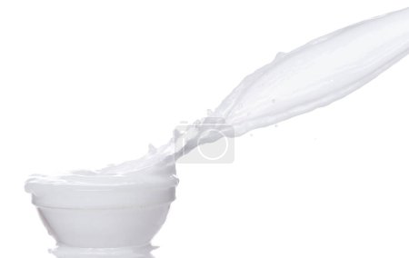 Téléchargez les photos : Le yaourt au lait déverse de l'eau blanche dans le bol. Lait lotion verser flotter dans l'air milieu. Lait hydratant explosion jeter flottement. fond blanc isolé haute vitesse obturateur gel mouvement - en image libre de droit