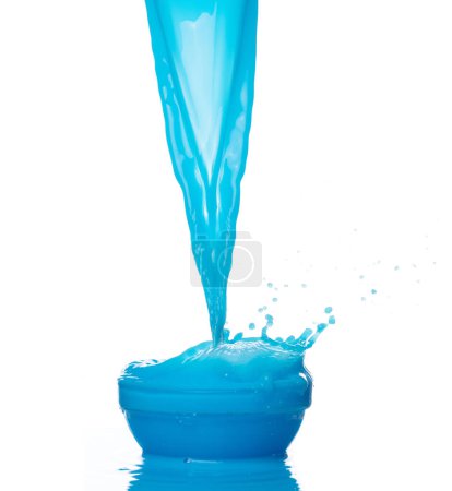 Foto de Derrame de agua de pintura azul salpicadura en taza del tazón. Loción líquida azul hidratante cosmético verter flotador en el aire. Bebida azul cóctel explosión lanzar aleteo. Fondo blanco aislado obturador de alta velocidad - Imagen libre de derechos