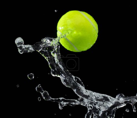 Téléchargez les photos : Balle de tennis a frappé l'eau et éclabousser dans l'air. Boule de tennis verte voler sous la pluie et éclabousser spin éclaboussure dans l'eau gouttelette. fond noir isolé gel action - en image libre de droit