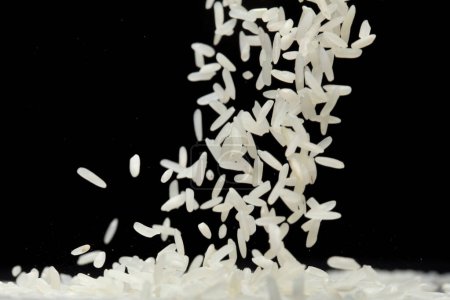 Téléchargez les photos : Riz japonais volant explosion, riz blanc grain rices tomber mouche abstraite. Belle graine complète de riz au jasmin éclaboussure dans l'air, conception d'objets alimentaires. Fond noir isolé foyer sélectif flou - en image libre de droit