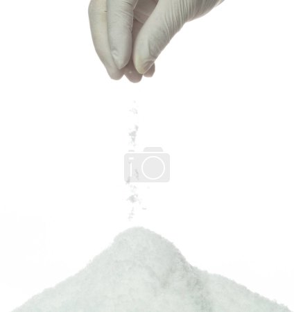 Téléchargez les photos : Le sel coulant tomber du doigt de la main, de grandes grandes fleurs de sels blancs explosent chute de nuage abstraite. tas de mélange de roche salée avec de la poudre moulue, conception d'éléments d'assaisonnement. Fond blanc isolé - en image libre de droit