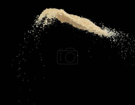 Foto de Brown Sugar explosión voladora, azúcar de grano marrón explotan mosca nube abstracta. Hermosa semilla completa salpicadura de caña de azúcar en el aire, diseño de objetos alimenticios. Congelación de enfoque selectivo tiro Fondo negro aislado - Imagen libre de derechos
