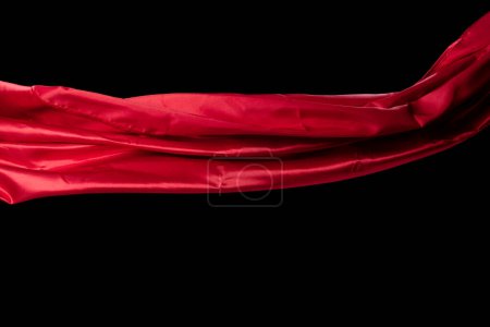 Téléchargez les photos : Tissu satin rouge volant en courbe, morceau de tissu satin rouge textile jeter tomber dans l'air. Fond noir flou de mouvement isolé - en image libre de droit