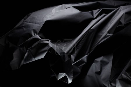 Arruga negra mussed tela volando en forma de curva, pieza de textil arruga negra mussed tela lanzar caída en el aire. Fondo negro aislado, entorno de sombra oscura