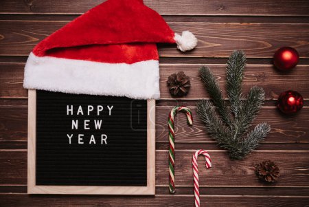 Photo for Happy New Year inscription on a letter board in New Year decorations, Santa hat, fir branches, cones, balls, caramel canes. Top view. Christmas card - Royalty Free Image