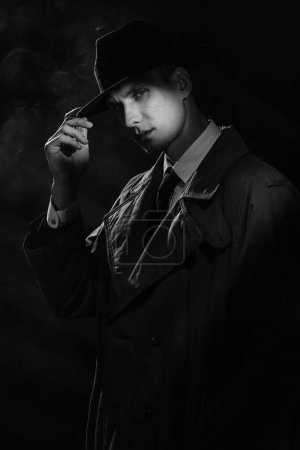 Foto de Una silueta oscura de un hombre con un impermeable y un sombrero al estilo del negro del crimen. Un dramático retrato negro al estilo de los detectives de los años 50 - Imagen libre de derechos