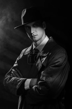 Foto de Una silueta oscura de un hombre con un impermeable y un sombrero al estilo del negro del crimen. Un dramático retrato negro al estilo de los detectives de los años 50 - Imagen libre de derechos