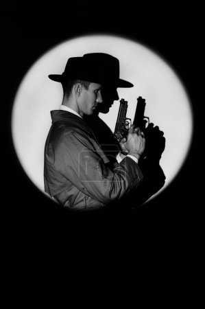 Foto de A dark silhouette of a male detective in a coat and hat with a gun in his hands in the noir style. A dramatic portrait in the style of detective films of the 1950s. The silhouette of a spy in a circle - Imagen libre de derechos