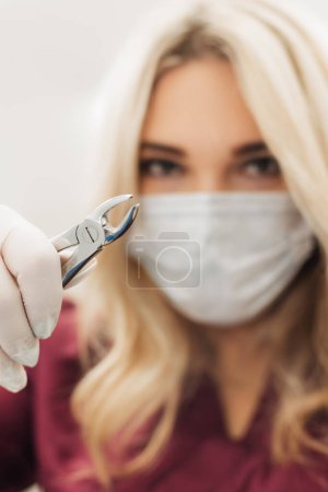 The dentist holds surgical pliers in his hands to remove a decaying tooth in the clinic. vertical photo