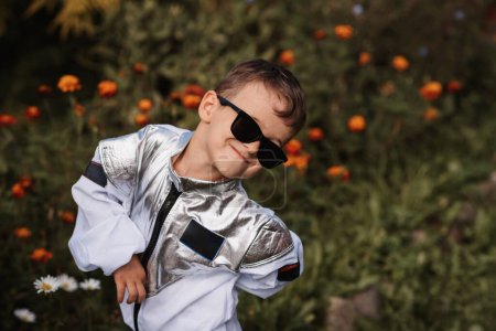 Ein kleiner Junge im Astronautenkostüm spielt an einem sonnigen Tag im Freien, umgeben von Blumen.