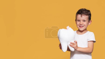 Un niño sonriente con dientes sanos sostiene un diente de felpa en sus manos sobre un fondo aislado. Higiene oral. Odontología pediátrica. Prevención de la caries. Un lugar para tu texto