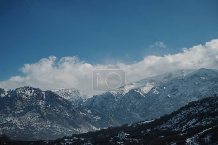 Panoramic view of snow-capped mountains against a blue cloudy sky