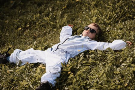 Ein kleiner Junge im Astronautenkostüm spielt draußen auf einem Feld an einem sonnigen Tag.