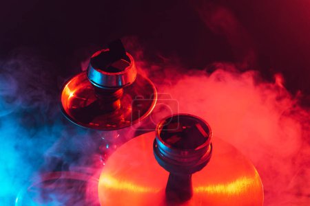 Téléchargez les photos : Narguilé bol, shisha et charbons gros plan sur fond noir fumé avec éclairage coloré - en image libre de droit