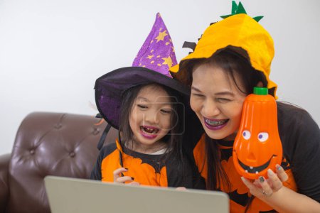 Téléchargez les photos : Mère heureuse et fille en costume de sorcière regarder réunion d'ordinateur avec un ami. - en image libre de droit