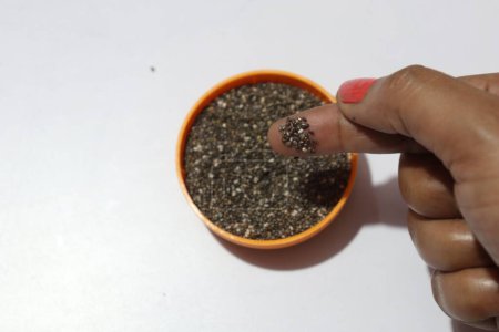 Téléchargez les photos : Femelle main vérifier les graines de chia dans un bol sur blanc - en image libre de droit