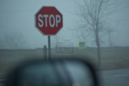 stop sign on the road on a dark day in the fog