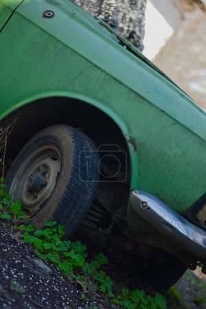 old green car, wheels partially covered with weeds and earth, abandoned vehicle