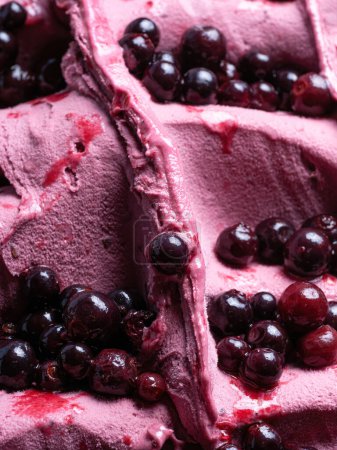 Téléchargez les photos : Frozen Black Elderberry flavour gelato - détail plein cadre. Gros plan d'une texture rose de crème glacée recouverte de morceaux de fruits rouge foncé. - en image libre de droit